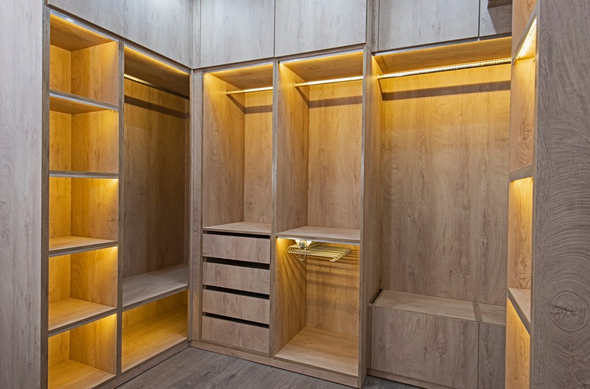 A walk-in wardrobe in light timber, each shelf and hanging rail lit by warm LED strip lighting