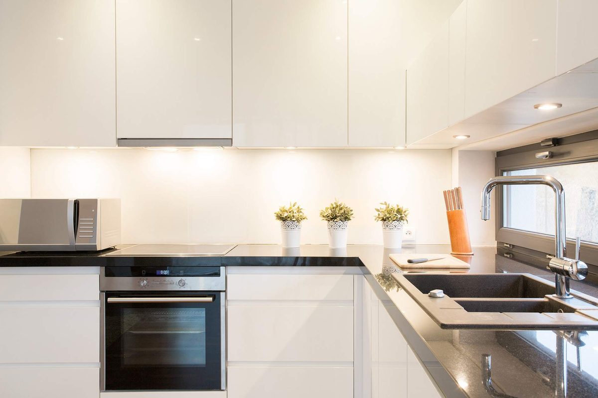A white kitchen with glossy cupboards, a wall oven, a black benchtop lit by under-cabinet lights and recessed downlights in the ceiling